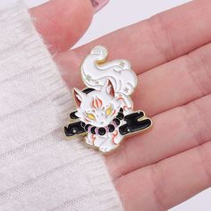 a hand holding a white and black enamel pin with an image of a cat on it