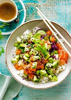 a bowl filled with rice, carrots and cucumbers next to chopsticks