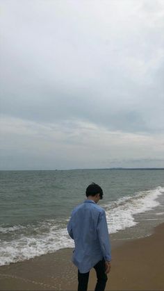 a man standing on top of a sandy beach next to the ocean under a cloudy sky