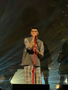 a man standing on top of a stage with a microphone in his hand and lights behind him