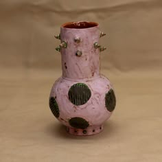 a pink vase with green polka dots and rivets on the outside, sitting on a tan surface