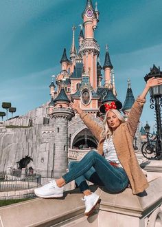 a woman sitting on the edge of a stone wall in front of a disney castle