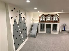 a play room with a slide and climbing wall in the corner, next to a house shaped like a mountain