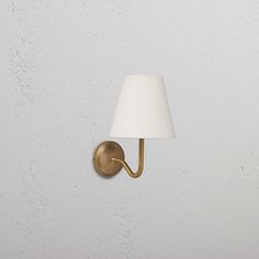 a wall light with a white shade on it's side and a gold arm