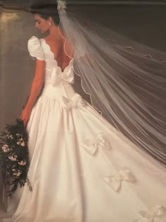 a woman wearing a wedding dress and holding a bouquet in front of her back with veil over her shoulder