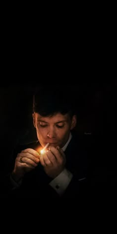 a man in a suit is lighting a candle with one hand and looking down at the other