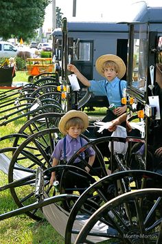 two young boys are sitting in an old fashioned wagon with wheels on the grass and another boy is wearing a straw hat