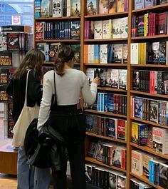 two women looking at books in a book store with the shelves full of books behind them