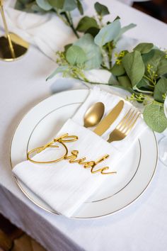 the table is set with white plates and gold utensils