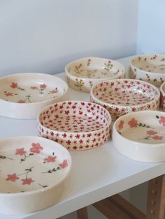 many white bowls with red flowers on them sitting on top of a table next to each other