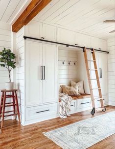 a living room with white walls and wooden floors, a ladder leading up to the bed