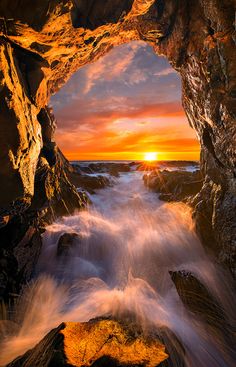 the sun is setting in an ocean cave with waves coming out from it and crashing into the rocks