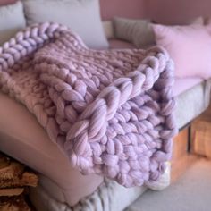 a blanket that is laying on top of a couch next to pillows and firewood