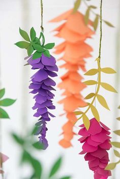 paper flowers hanging from strings in front of a white wall with green leaves on it