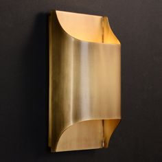 a gold metal object mounted on the wall with a black back ground and dark walls behind it