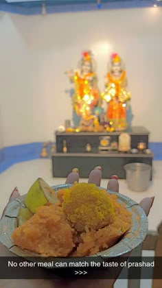 a person holding a plate with food on it in front of a small buddha statue