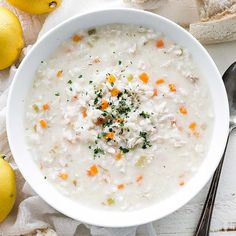 a white bowl filled with soup next to lemons and bread on top of a table