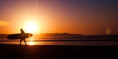 a person with a surfboard walking on the beach at sunset