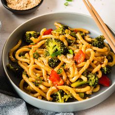 a bowl filled with noodles, broccoli and peppers next to chopsticks