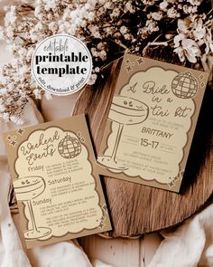 two brown and white wedding cards sitting on top of a wooden table next to flowers