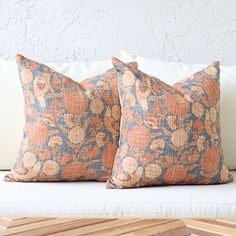 two orange and blue pillows sitting on top of a white couch next to each other