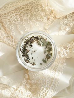 an overhead view of a glass cup with herbs in it on a lace tablecloth