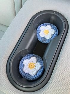 two crocheted flowers are placed in the center console of a car, on top of a black tray