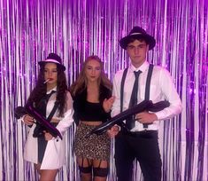 three people dressed in costume posing for a photo with purple tinsel backdrop behind them