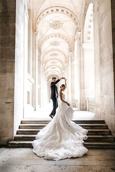 a bride and groom posing for a photo on the stairs in an old building with stone arches