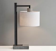 a table lamp with a white shade on it and a black metal frame around the base