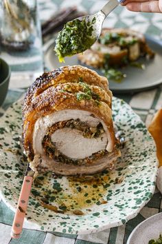 a person holding a knife and fork over a meat roll on a plate with broccoli