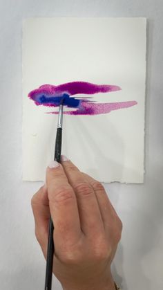 a person is holding a brush and painting on paper