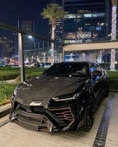 a black sports car parked in front of a tall building at night with palm trees