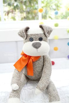 a stuffed dog with an orange ribbon around its neck sitting on a bed in front of a window