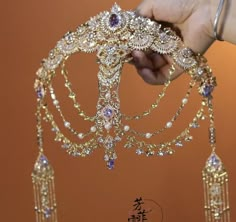 a hand is holding a gold tiara with purple and white stones on it's sides