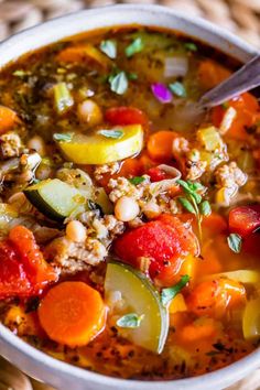 a white bowl filled with vegetable soup on top of a wicker tablecloth next to a spoon