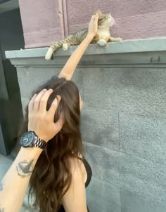 a woman reaching up to pet a cat on the side of a building with her hand