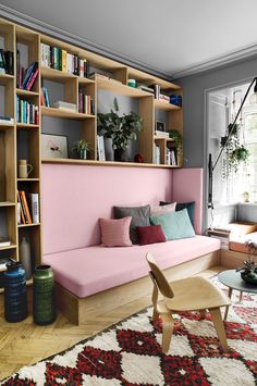 a living room with a pink couch and bookshelf in the corner, next to a window