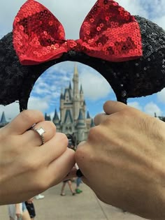 someone is holding their engagement ring in front of mickey mouse ears with the castle in the background