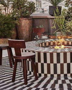 an outdoor fire pit in the middle of a tiled patio with potted plants around it