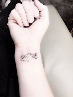 a woman's arm with a small tattoo on the wrist and mountains in the background