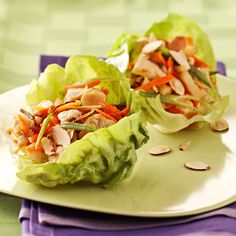 two lettuce wraps filled with vegetables on a white plate next to blue napkins