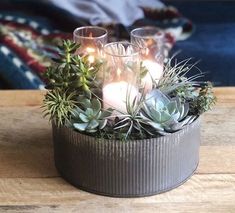 some candles are sitting in a metal container with succulents