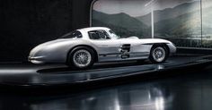 a silver sports car is on display in a dark room with mountains and trees behind it