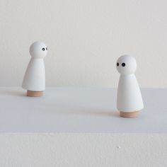 two small white figures sitting on top of a table next to each other with eyes