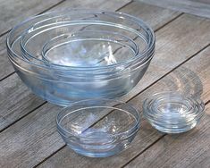 three clear glass bowls and one empty bowl are sitting on a wooden table with the lids down