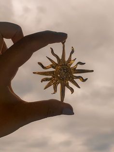 a hand holding a gold sun ornament against a cloudy sky