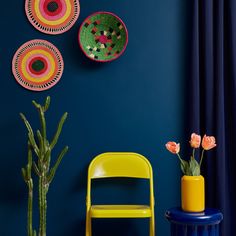 three colorful plates hanging on the wall next to a yellow chair and potted plant