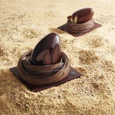 two chocolate eggs sitting on top of each other in a nest made out of sand