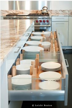 an open drawer in the middle of a kitchen with plates and bowls on it's sides